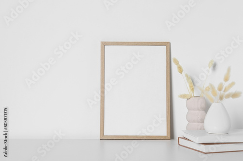 Empty photo frame and vases with dry decorative spikes on white table. Mockup for design