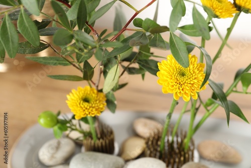 Ikebana art. Beautiful yellow flowers and green branches on table