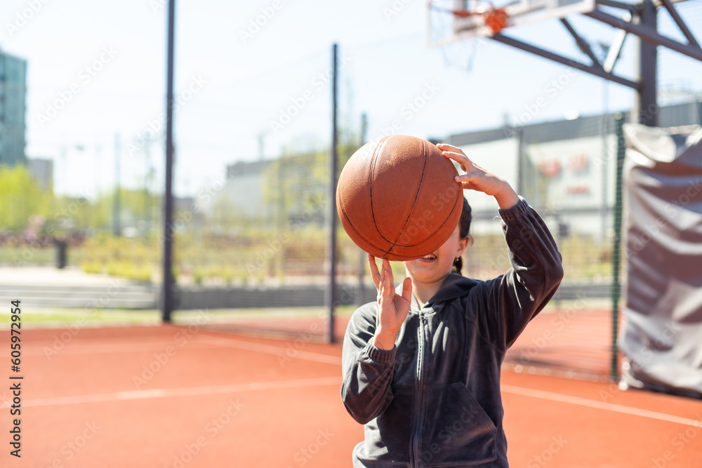 Naklejka premium A girl with basketball on court on summer season.