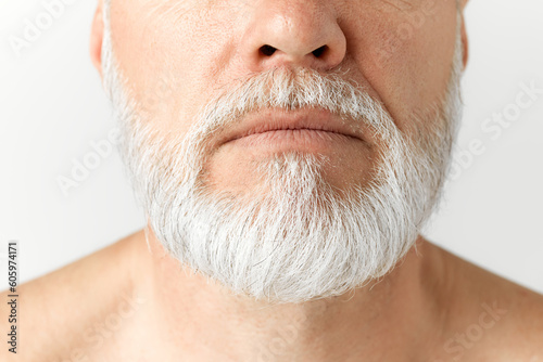 Cropped close-up image of grey-haired man's beard. Taking care after hair and beard. Mature male model against grey background. Concept of male beauty, face and skin care, daily procedures, age