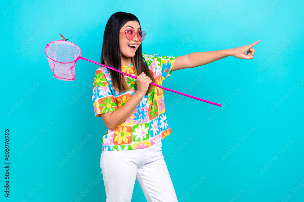 Photo of cute excited lady wear flower print t-shirt pink eyewear holding scoop pointing empty space isolated blue color background Photo of cute excited lady wear flower print t-shirt pink eyewear holding scoop pointing empty space isolated blue color background