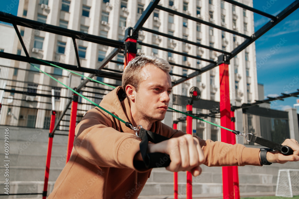 A young man, focused and energetic, is exercising with resistance bands outdoors. A young man, focused and energetic, is exercising with resistance bands outdoors.