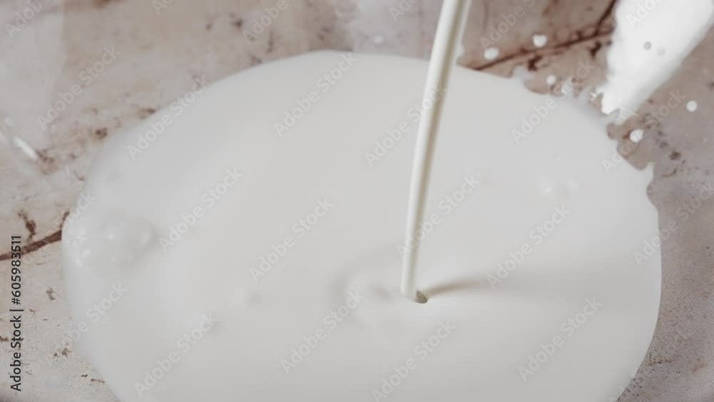 Slow-motion closeup of cream being poured down to a glass bowl Slow-motion closeup of cream being poured down to a glass bowl