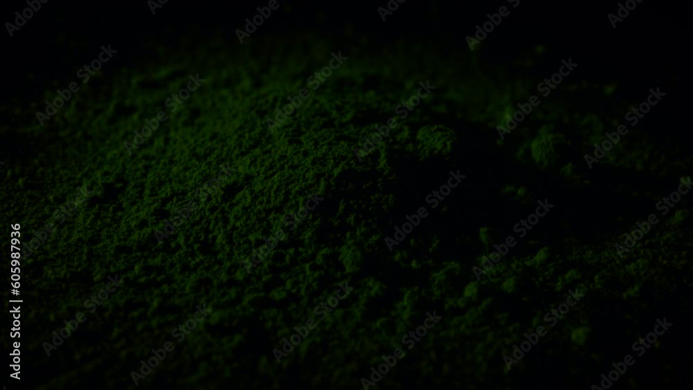 Scattered matcha tea powder on a black surface with fading at the beginning and at the end