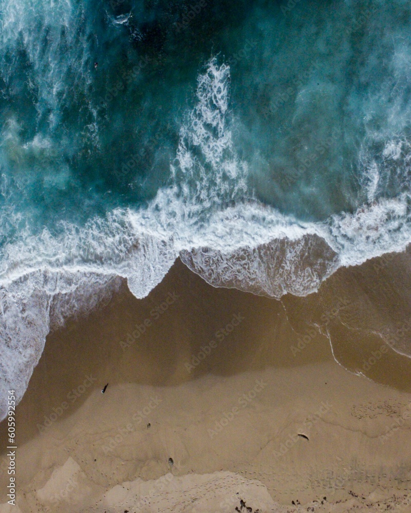 Scenic vertical aerial top view of blue sea waves touching the sandy coast Scenic vertical aerial top view of blue sea waves touching the sandy coast