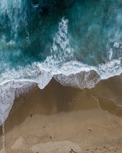 Scenic vertical aerial top view of blue sea waves touching the sandy coast