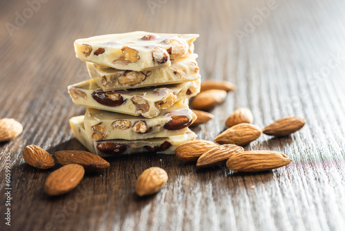 White broken chocolate bars with almonds on wooden table.