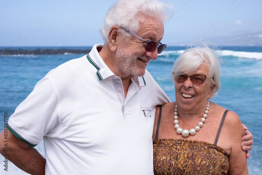 Happy senior family couple hugging enjoying sea vacation and freedom in a sunny day. Retirement lifestyle concept