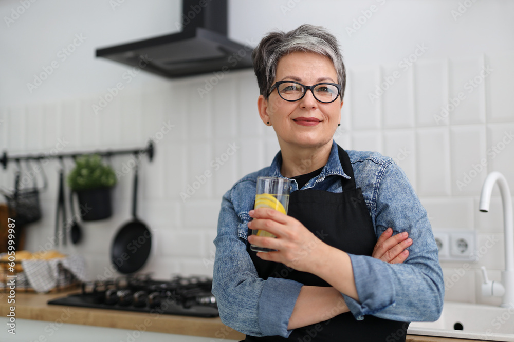Φωτογραφία Smiling senior woman in glasses holds a glass of lemon water in her hands