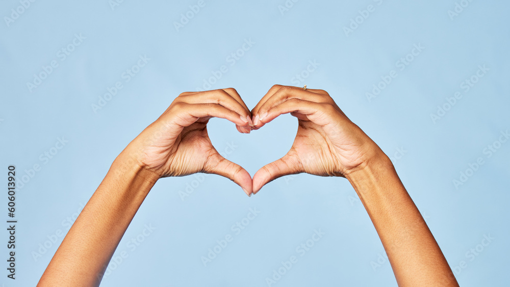 Obraz premium Hands, heart and emoji with a person in studio on a blue background for love, health or social media. Affection, romantic and hand gesture with an adult indoor to show a sign or icon of romance