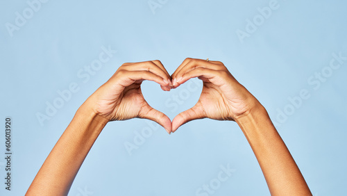 Hands, heart and emoji with a person in studio on a blue background for love, health or social media. Affection, romantic and hand gesture with an adult indoor to show a sign or icon of romance