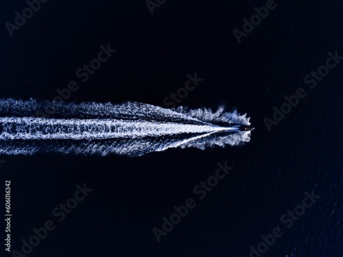 Aerial top view of a boat sailing in the water leaving a trail © Pavlicc/Wirestock Creators