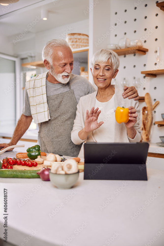 Smiling elderly vegan couple preparing a fresh vegetable salad in the kitchen, using a tablet Smiling elderly vegan couple preparing a fresh vegetable salad in the kitchen, using a tablet