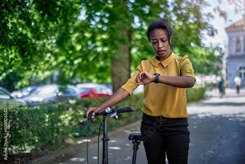 Young woman with a bicycle checking the time on her wristwatch. 