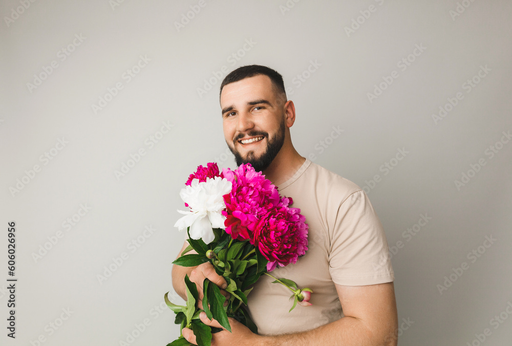 image of a handsome man with a bouquet of pink peonies as a gift. Smiling man with flowers, isolated on a gray background. image of a handsome man with a bouquet of pink peonies as a gift. Smiling man with flowers, isolated on a gray background.