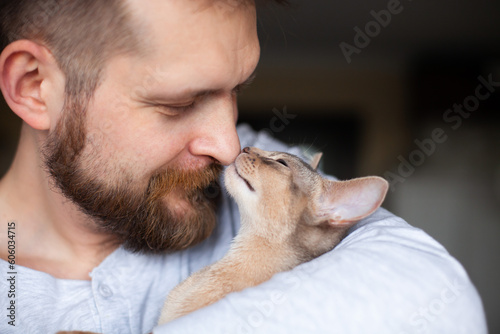 Close up of abyssinian kitten cuddling bearded man's nose. Tenderness, friendship between human and cat. Pets care. World cat day. Selective focus.