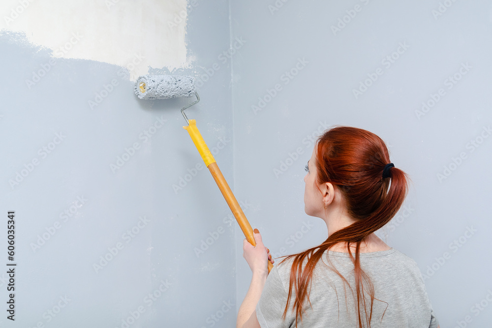 Portrait of young adult girl with red hair,woman painting walls with a gray brush roller,living,bedroom,moving to new apartment.Female artist, interior decorator, repair of a residential apartment Portrait of young adult girl with red hair,woman painting walls with a gray brush roller,living,bedroom,moving to new apartment.Female artist, interior decorator, repair of a residential apartment