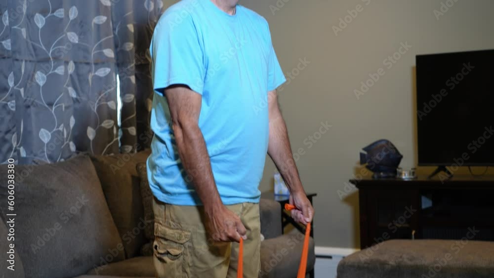 A tilt up medium shot view of a man using a rubber exercise band in his living room at home. A tilt up medium shot view of a man using a rubber exercise band in his living room at home.
