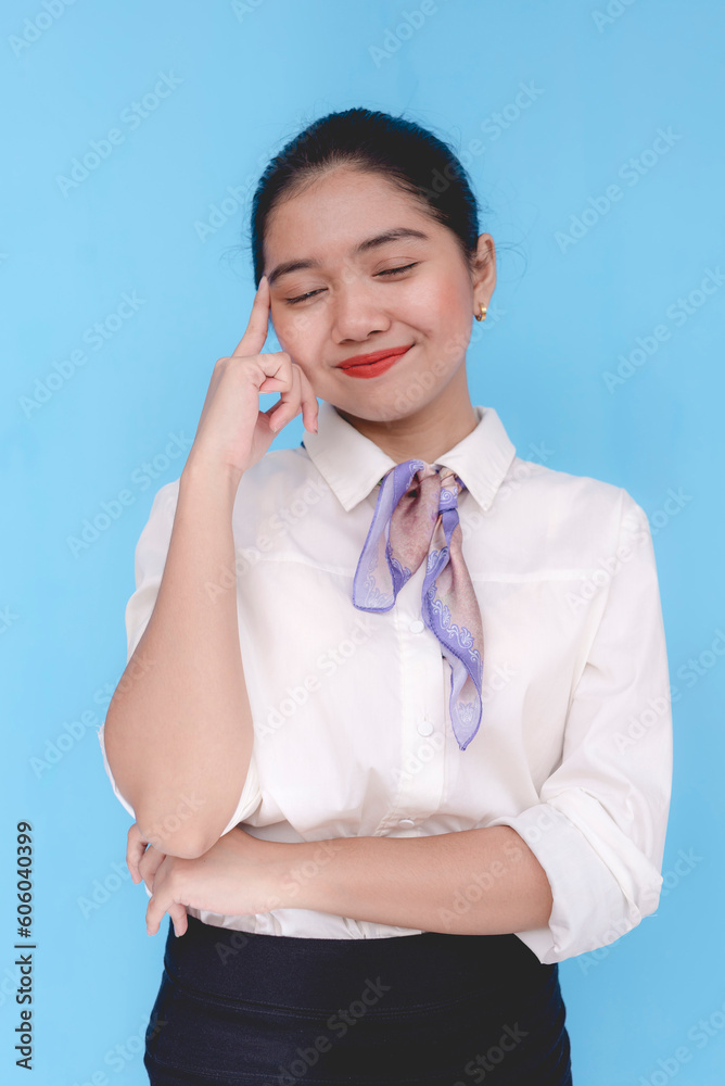 A flight attendant or stewardess thinking and pondering about something. A hostess with her index finger pointed on her head while her eyes are closed. Isolated on a blue background. A flight attendant or stewardess thinking and pondering about something. A hostess with her index finger pointed on her head while her eyes are closed. Isolated on a blue background.