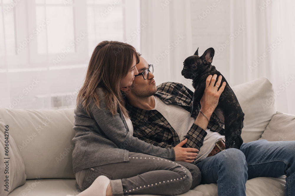 Happy couple is having fun and playing with their French Bulldog puppy at home.Family and animal life concept. Happy couple is having fun and playing with their French Bulldog puppy at home.Family and animal life concept.