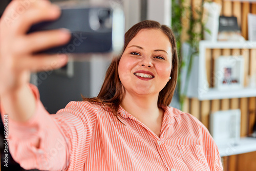 A smiling curvy woman wearing a nice striped shirt and taking a selfie with a mobile phone.