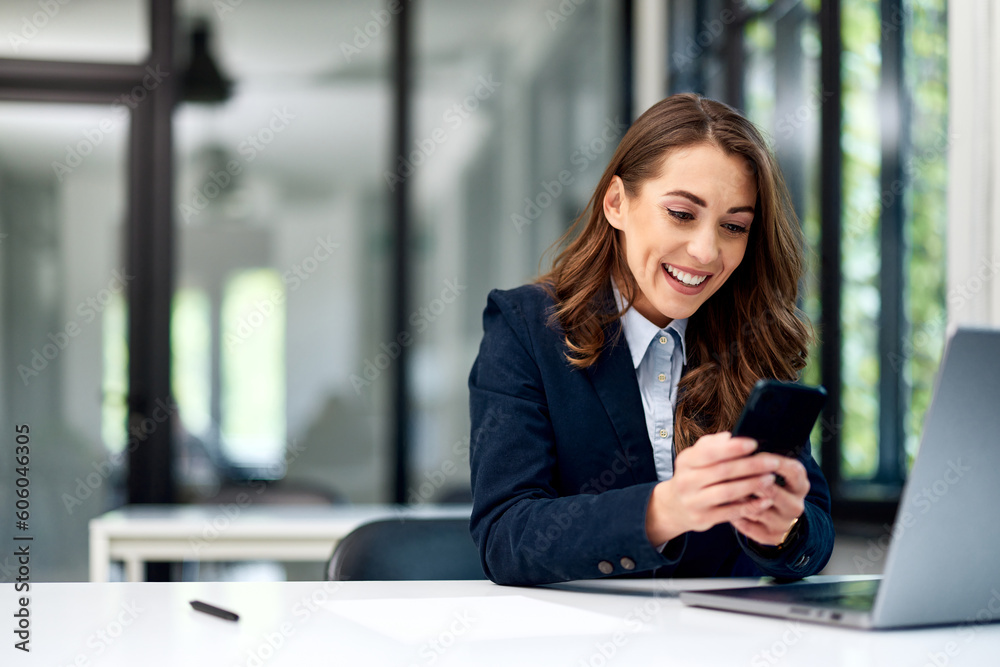 A smiling businesswoman typing messages on a mobile phone while working on a laptop. A smiling businesswoman typing messages on a mobile phone while working on a laptop.