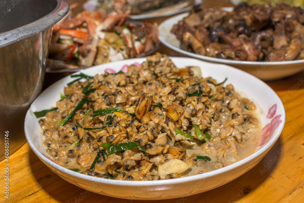 Close-up on cooked clams. Southern Chinese festivity rural food on bowls and plates at a wooden table. Close-up on cooked clams. Southern Chinese festivity rural food on bowls and plates at a wooden table.