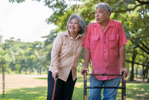 An old elderly Asian man uses a walker and walks in the park with his wife.  Concept of happy retirement With Love and care from family and caregiver, Savings, and senior health insurance © Prot
