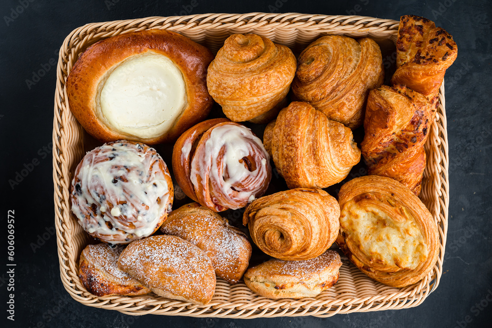 Fresh pastries: croissants, rolls, puffs and bun with sour cream in basket.