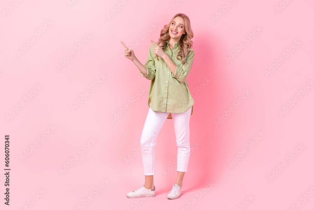Full length portrait of cheerful nice person direct fingers look empty space offer isolated on pink color background Full length portrait of cheerful nice person direct fingers look empty space offer isolated on pink color background