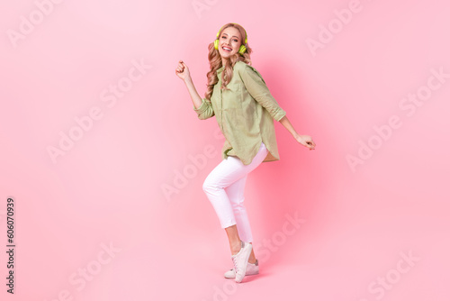 Full length photo of excited pretty woman dressed green shirt earphones dancing having fun isolated pink color background