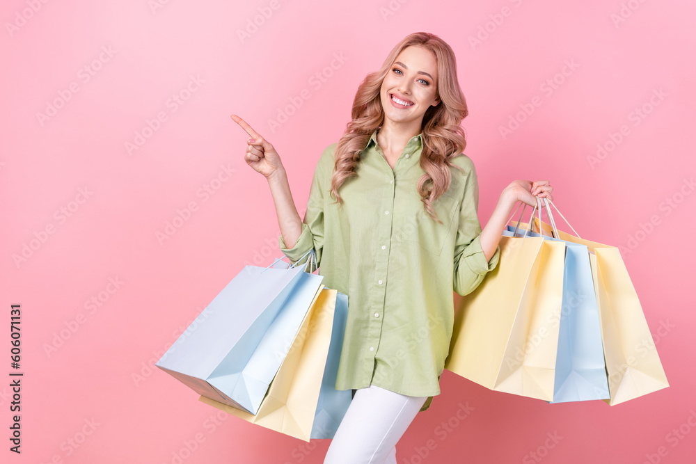 Photo of cute shiny woman dressed green shirt holding bargains showing finger empty space isolated pink color background
