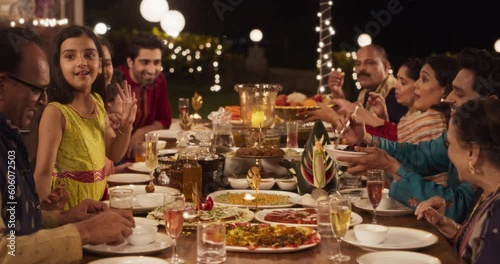 Happy Indian Family Having a Feast and Celebrating Diwali Together: Group of People of Different Ages in Their Traditional Clothes Eating Dinner Together in a Backyard Garden, Talking and Laughing