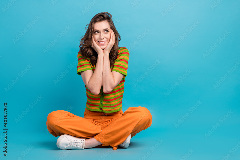 Full size photo of minded woman dressed orange pants colorful cardigan look empty space arms cheekbones isolated on blue color background Full size photo of minded woman dressed orange pants colorful cardigan look empty space arms cheekbones isolated on blue color background