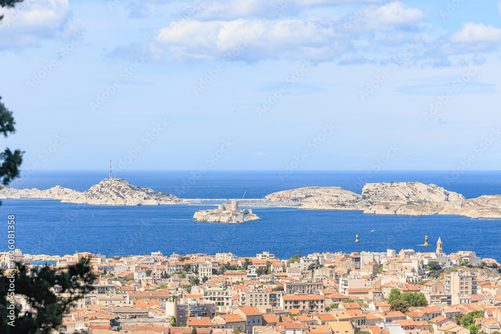 A scenics aerial view of the city of Marseille, bouches-du-rhône, France with rocky island in the background at the port under a majestic blue sky and some white clouds