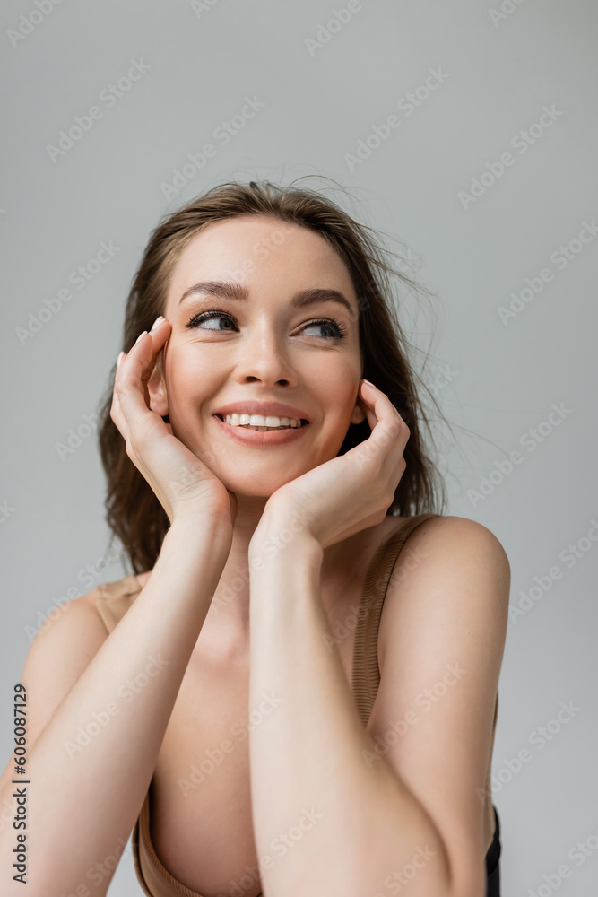 Portrait of cheerful and sexual young brunette woman with everyday makeup wearing bodysuit and looking away while posing isolated on grey, hands near face Portrait of cheerful and sexual young brunette woman with everyday makeup wearing bodysuit and looking away while posing isolated on grey, hands near face