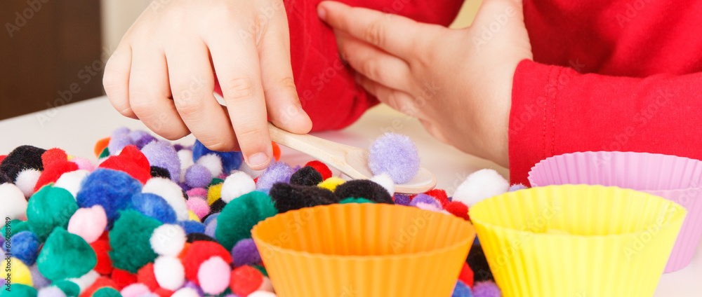 Preschooler playing with small pompoms, wooden spoon and cups. Development of kids motor skills, coordination and logical thinking Preschooler playing with small pompoms, wooden spoon and cups. Development of kids motor skills, coordination and logical thinking