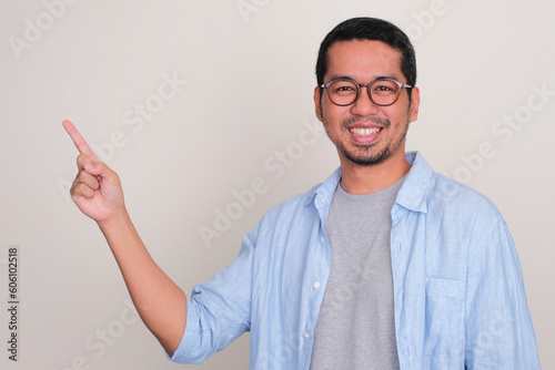 Adult Asian man smiling confident with one hand pointing to the right side
