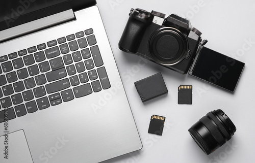 Laptop, Modern digital camera with flip screen, two sd memory cards, battery and lens on gray background. Photographer's equipment. Top view. Flat lay
