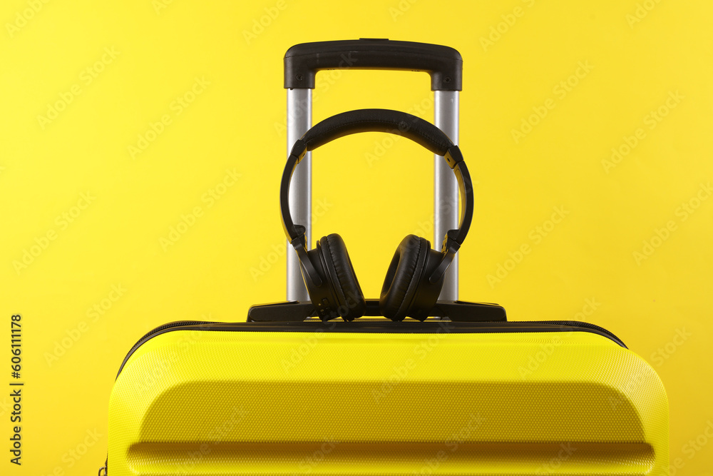 Yellow plastic travel suitcase, and stereo headphones on a yellow background. Tourism, vacation, relocation concept Yellow plastic travel suitcase, and stereo headphones on a yellow background. Tourism, vacation, relocation concept