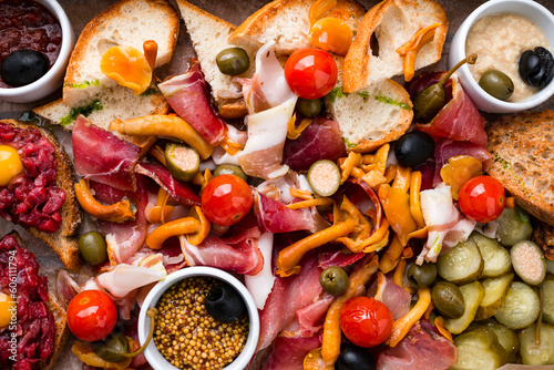 Fototapeta Naklejka Na Ścianę i Meble -  Background of banquet meat plate with slices of ham, olives, cherry tomatoes, honey mushrooms, pickled cucumbers, tar tar, mustard and bread.