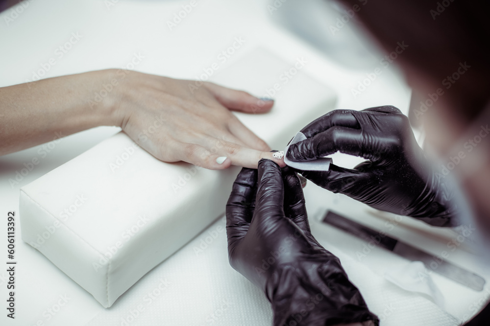 Fototapeta premium Manicurist files with nail file the nails of hands of woman client in nail salon