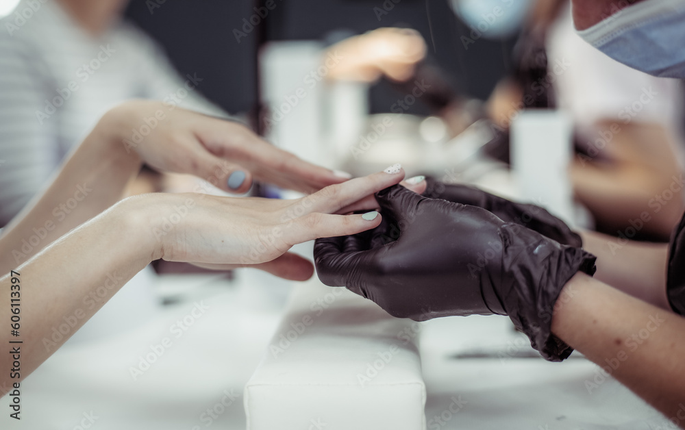 Manicurist in black gloves holds the hands of a woman client and examines the manicure done