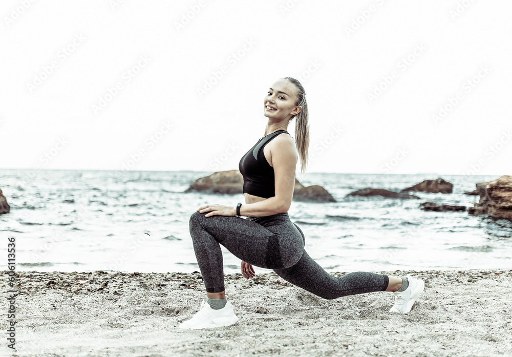 Beautiful young fit woman in sportswear practicing stretching legs alone on wild beach. Healthy lifestyle concept