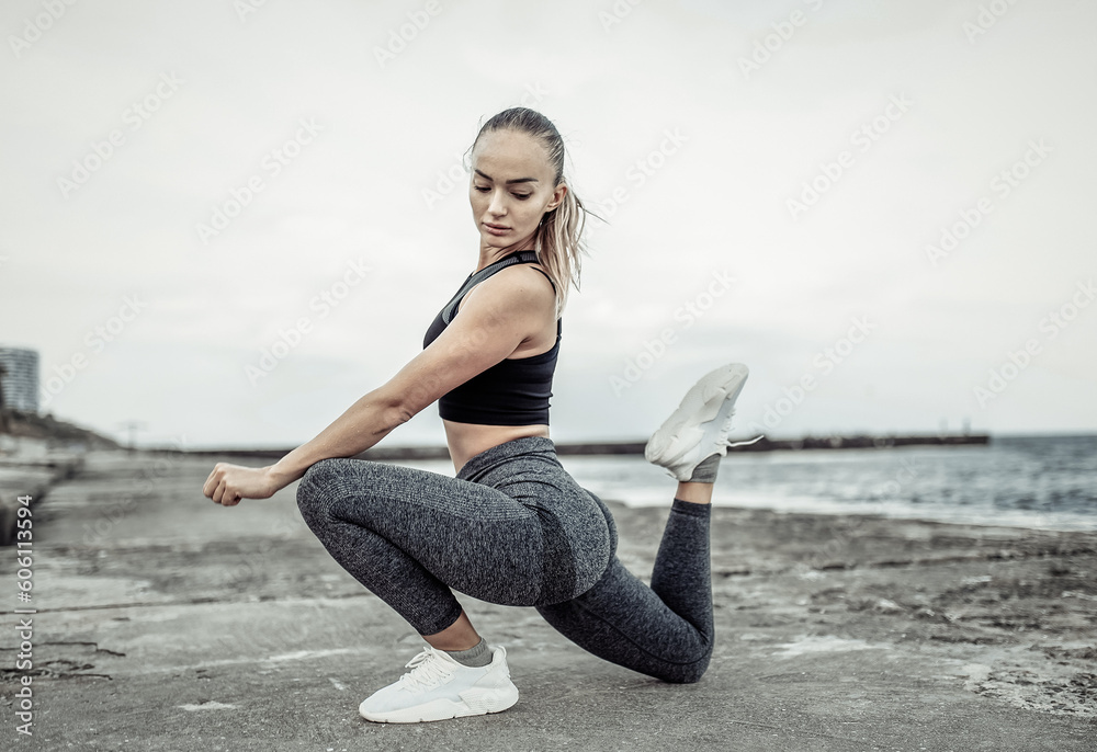Beautiful young fit woman in sportswear training alone on urban beach. Healthy lifestyle concept