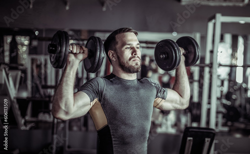 Athletic man exercising shoulder muscles with dumbbells in his hands