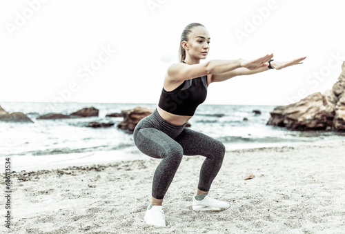 Beautiful young fit woman in sportswear practicing squats alone on wild beach. Healthy lifestyle concept