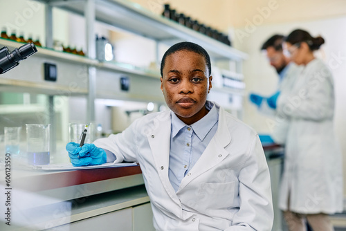 Black female microbiologist working in lab and looking at camera.