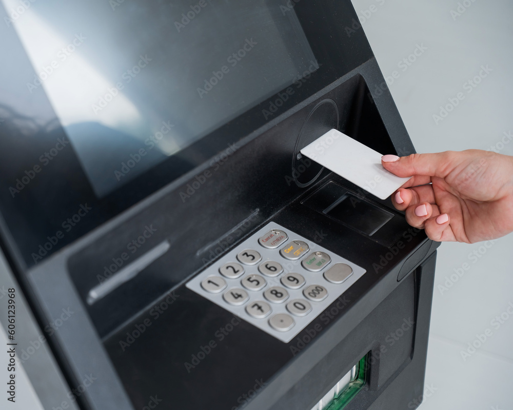 A faceless woman inserts a credit card into an ATM. Close-up of a woman's hands using an ATM machine. A faceless woman inserts a credit card into an ATM. Close-up of a woman's hands using an ATM machine.