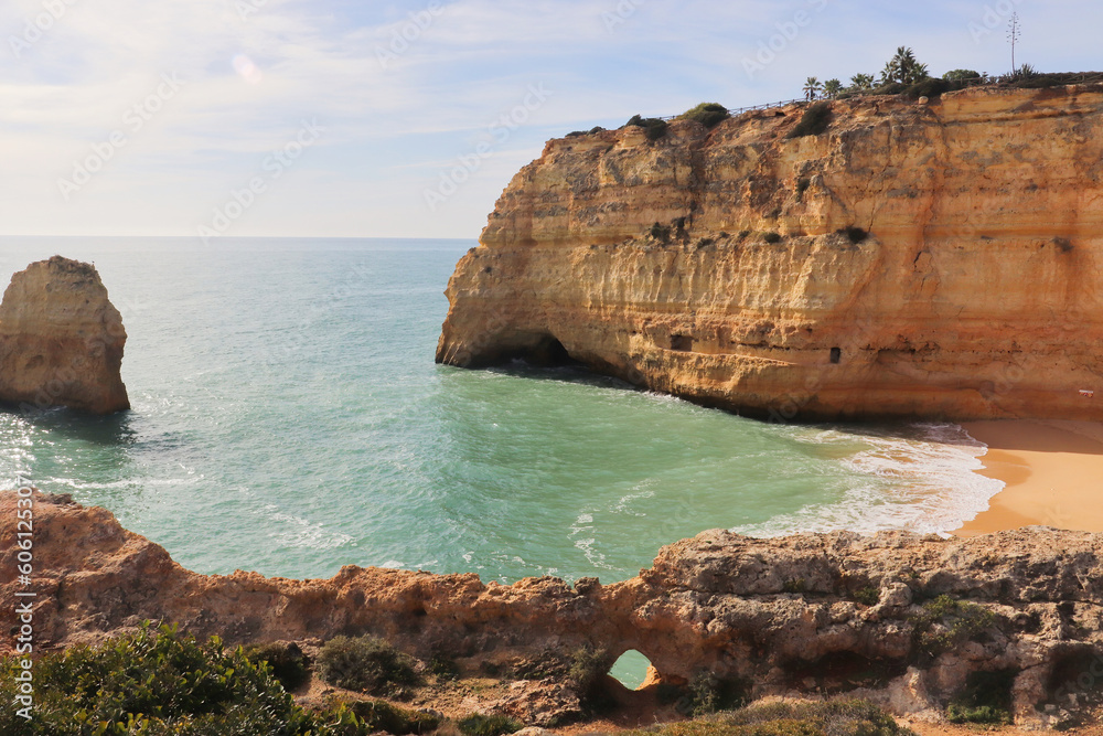 Small hole in a rock on the Seven Hanging Valleys Trail with limestone cliffs and sandy beaches next to the Atlantic Ocean on a sunny winter day in southern Portugal.